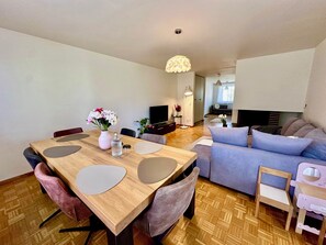 A modern living room with a wooden dining table, a sofa, and a TV.