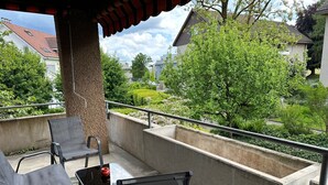 A balcony with two chairs and a small table, surrounded by a concrete wall and a railing.