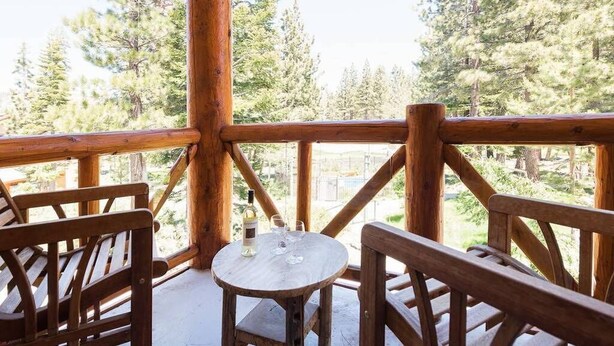Une terrasse en bois avec une table ronde et des bancs, donnant sur une zone boisée.