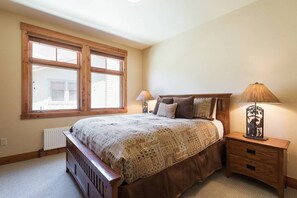 A bedroom with a large bed, two bedside lamps, a radiator, and a window with blinds. - Golf Course Property, Allows Pets, BBQ, Underground Parking, Laundry (Mammoth Lakes)