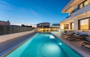 Ein Pool auf dem Dach mit Liegestühlen, einer überdachten Sitzgelegenheit und einem modernen Gebäude im Hintergrund.
