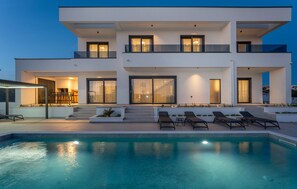 Ein modernes, zweistöckiges Haus mit Swimmingpool, Sitzgelegenheit im Freien und einer gut beleuchteten Eingangsparte.