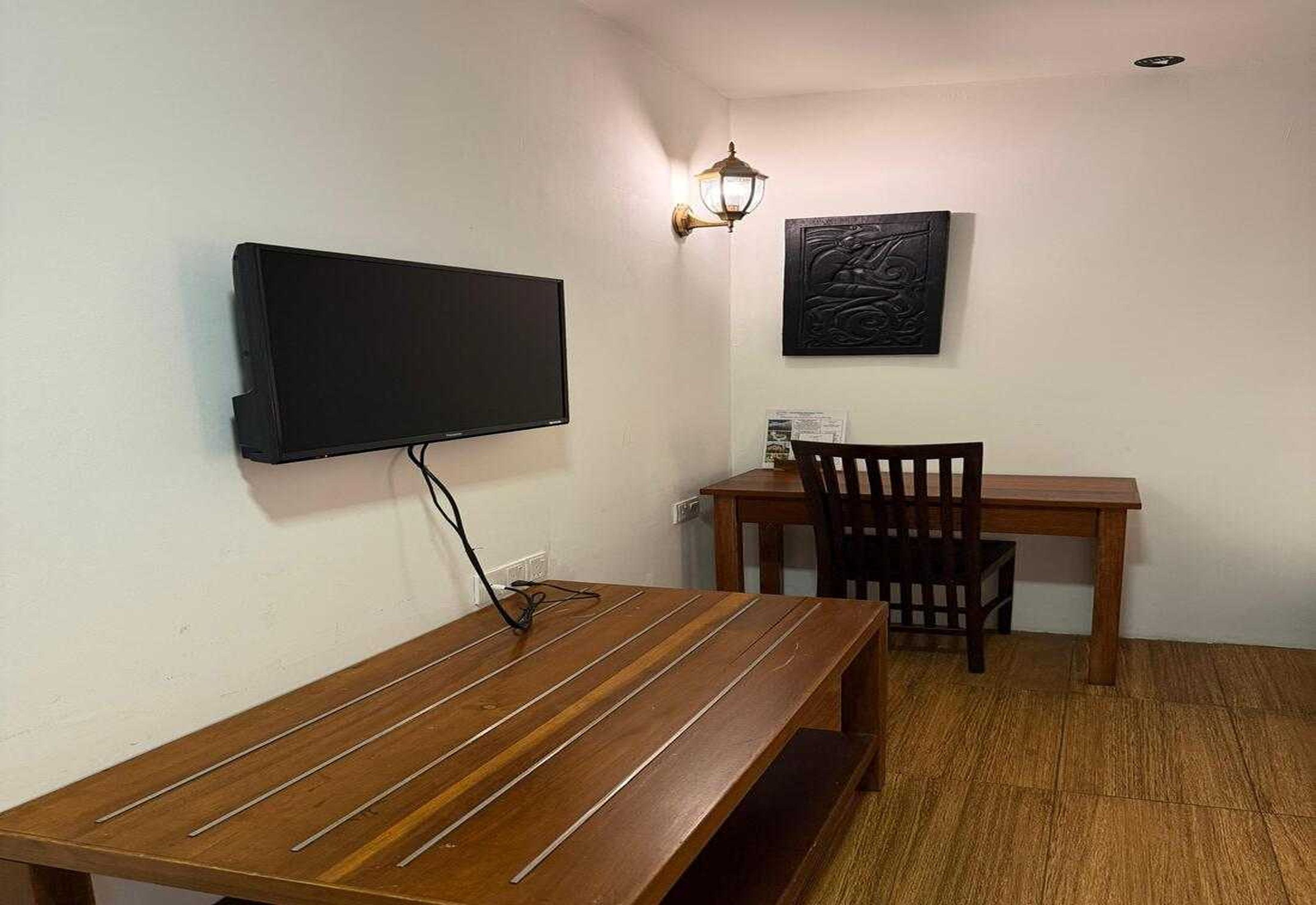 A room with a wooden table, a chair, a wall-mounted TV, and a decorative wall piece.
