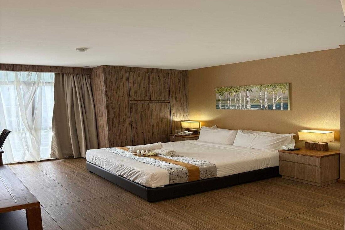 Habitación de hotel con una cama grande, dos mesitas de noche, un cuadro en la pared y vistas a través de la ventana.