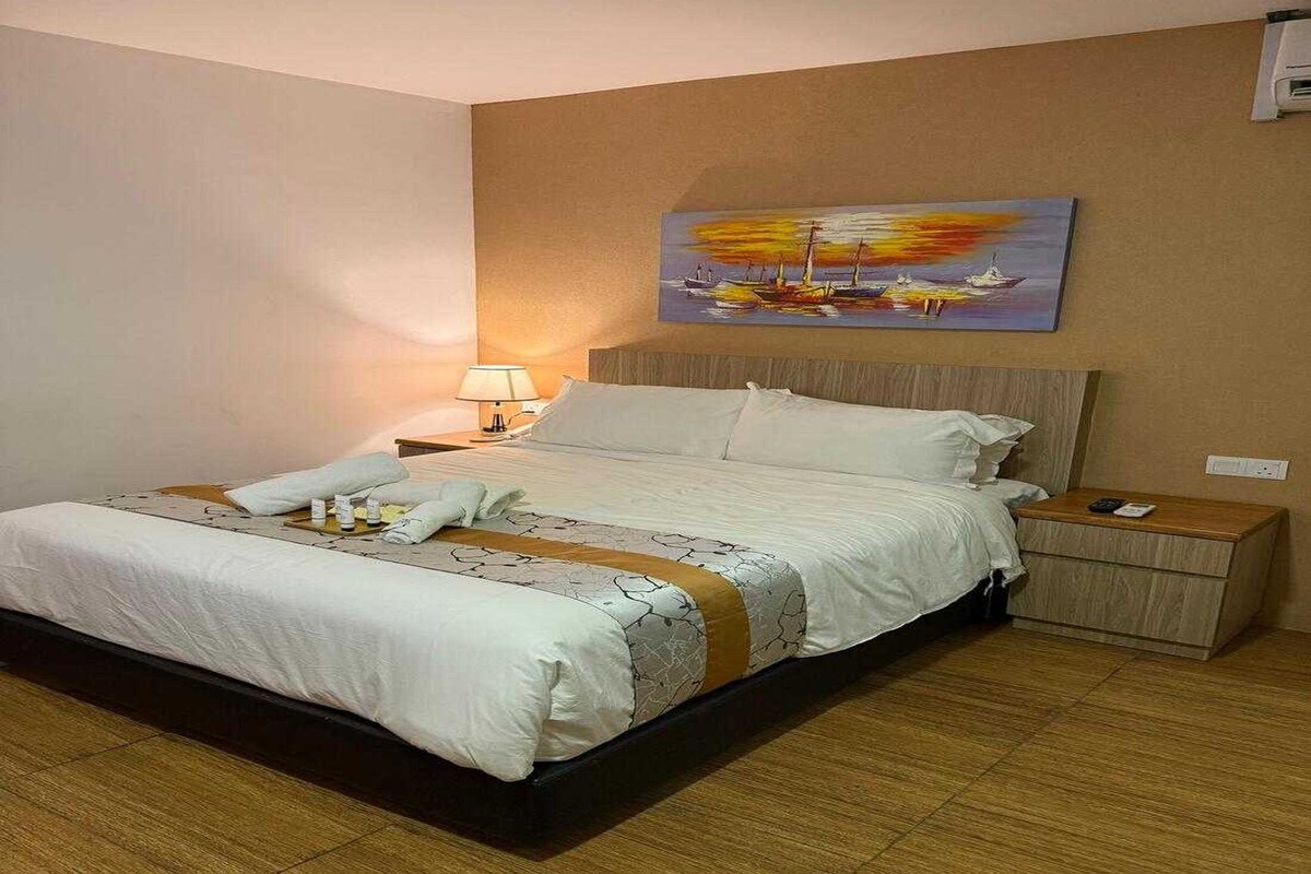 Una habitación de hotel con una cama, una mesita de noche, un cuadro y una lámpara.
