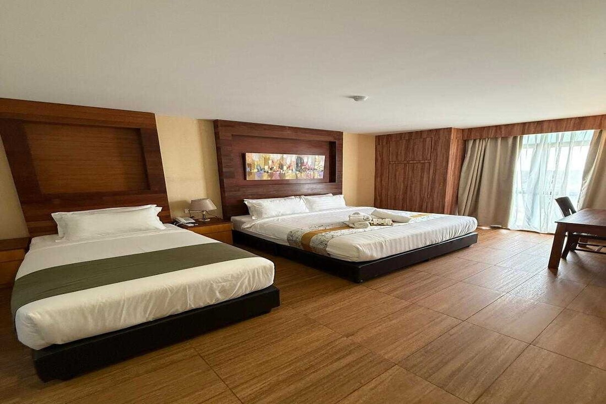 Habitación de hotel con dos camas, cabecero de madera, un cuadro sobre las camas y un amplio ventanal con cortinas.