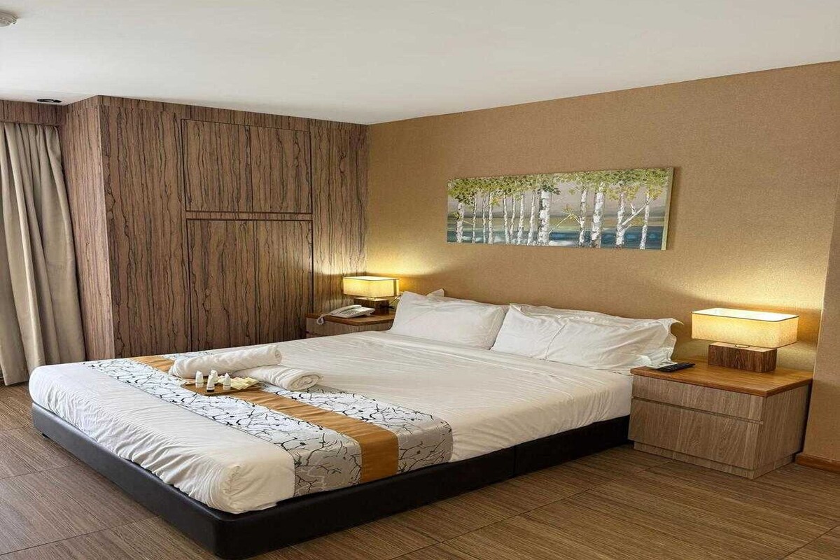 Habitación de hotel con una cama grande, dos mesitas de noche, un cuadro en la pared y un panel de pared de madera.
