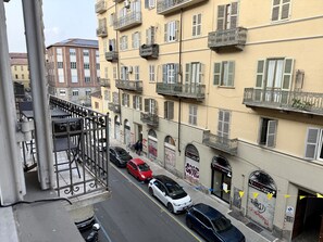Vista d'un carrer amb cotxes estacionats, un edifici amb balcons i un rètol de 'Massaggitina'.