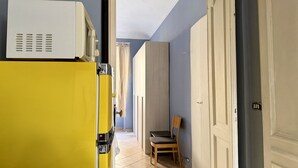 Un couloir avec un appareil de couleur jaune, une chaise en bois et une porte donnant sur une autre pièce.