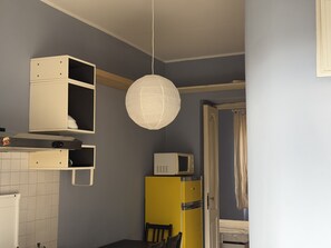 A compact kitchen with a microwave, a yellow refrigerator, and a hanging paper lantern. - Purple Nest House (Turin)
