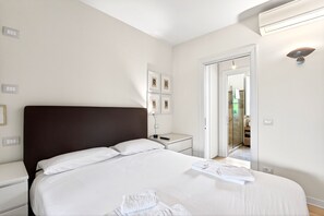 Una habitación de hotel con una cama grande, mesitas de noche, un espejo y una puerta que da a un baño.