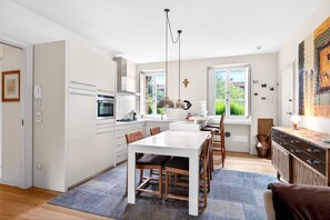 Une cuisine moderne avec des meubles blancs, une table à manger et des chaises, un four encastré et un luminaire suspendu.
