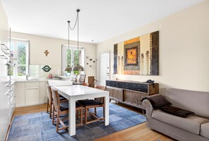 Une cuisine moderne avec des meubles blancs, une table à manger avec des chaises, un canapé et un grand tableau abstrait accroché au mur.