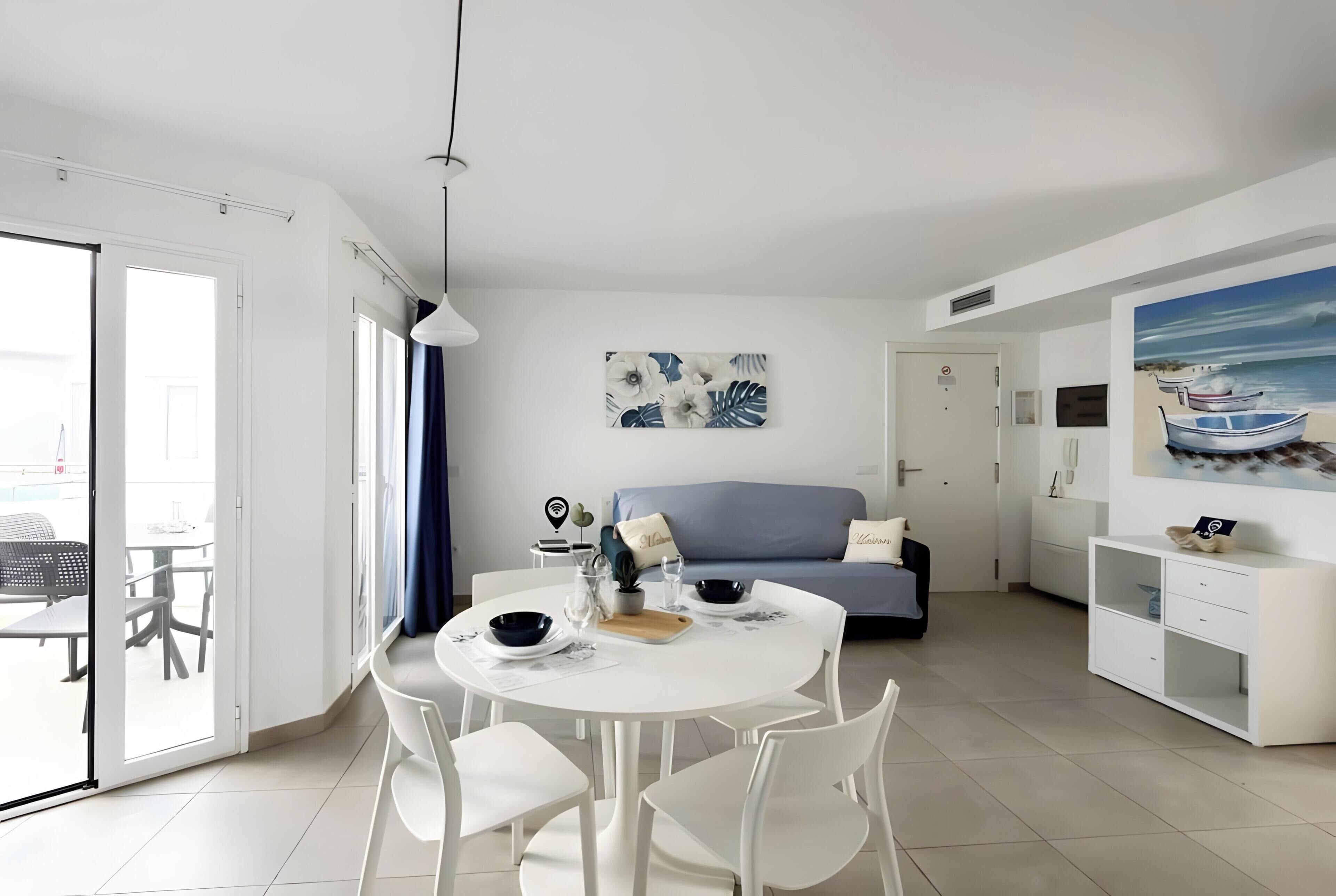 A modern, well-lit room with a dining table, chairs, a sofa, and artwork on the walls.
