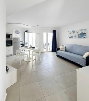 Een moderne woonkamer met een bank, eettafel, stoelen en een keuken met apparatuur.