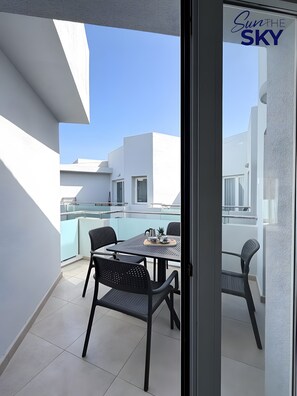 En balkon med et bord og stole, en klar himmel og en bygning med et skilt, der viser 'Sun the SKY'.