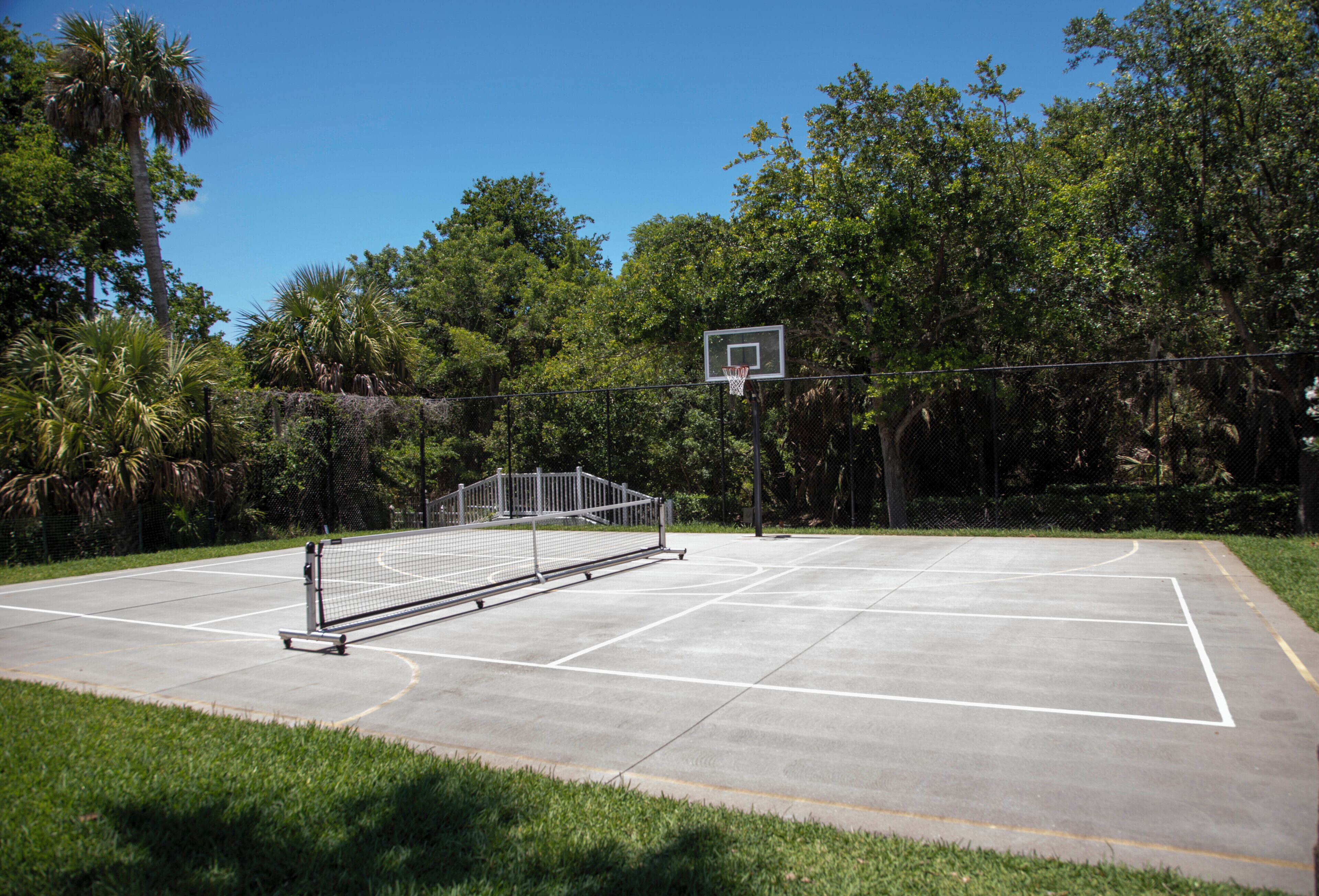 An outdoor basketball court with a net, surrounded by trees and a clear sky.