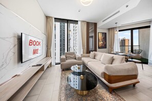 Ein modernes Wohnzimmer mit Sofa, Couchtisch, an der Wand montiertem Fernseher und Blick auf die Stadt durch große Fenster.