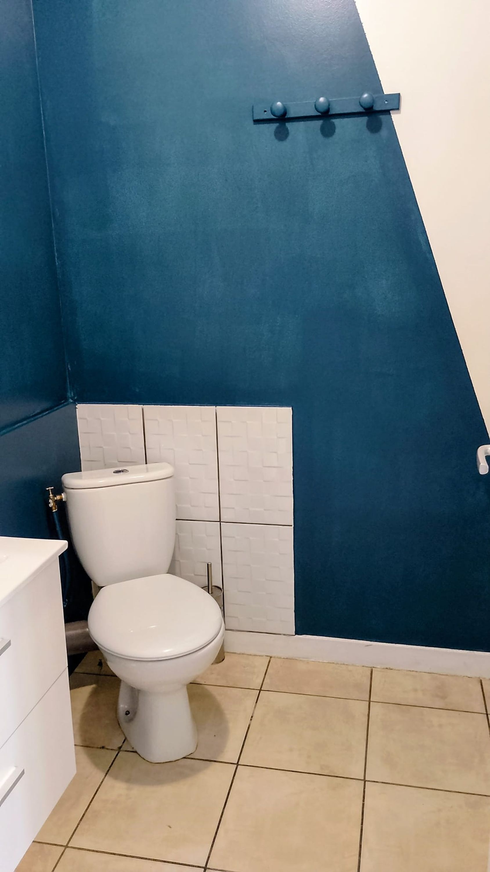 Et badeværelse med et hvidt toilet, blå væg og et hvidt flisebælte.