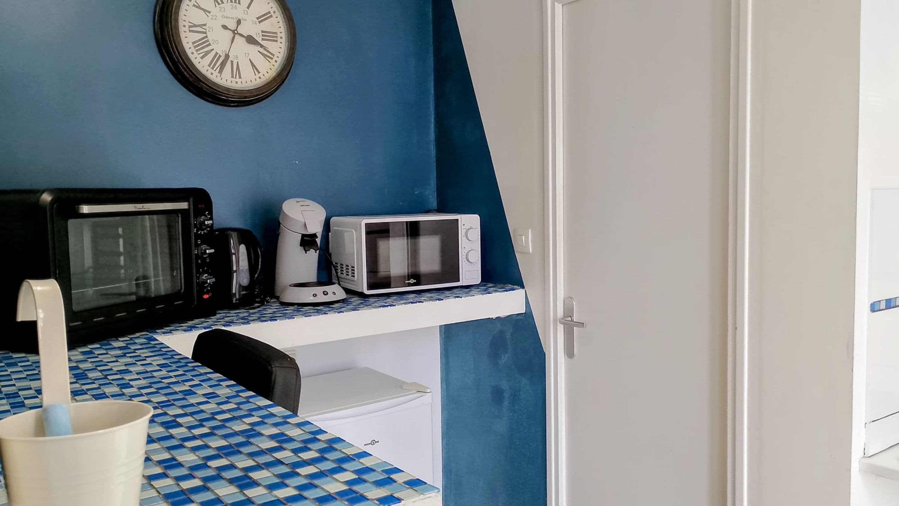 A kitchen with a microwave, toaster, coffee maker, and a clock on the wall.