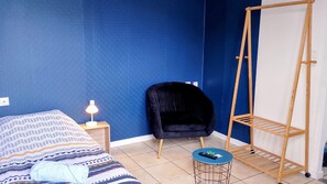 A bedroom with a bed, a chair, a standing desk, and a small table with a remote control. - Le Nouveau 101 Wifi Parking 1pers (Noeux-les-Mines)
