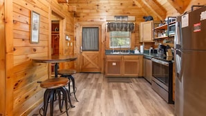 A wooden cabin interior with a kitchen, dining area, and a door leading to a closet. - Location Hot Tub Privacy Fireplace Common Pool (Gatlinburg)