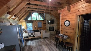 A cozy cabin interior with a dining area, kitchen, and seating space. - Location Hot Tub Privacy Fireplace Common Pool (Gatlinburg)