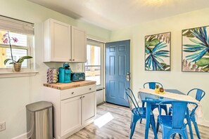 A kitchen with white cabinets, a blue door, and a dining area with blue chairs and a table. - Gulf Shores Beach Condo With Pool (Gulf Shores)