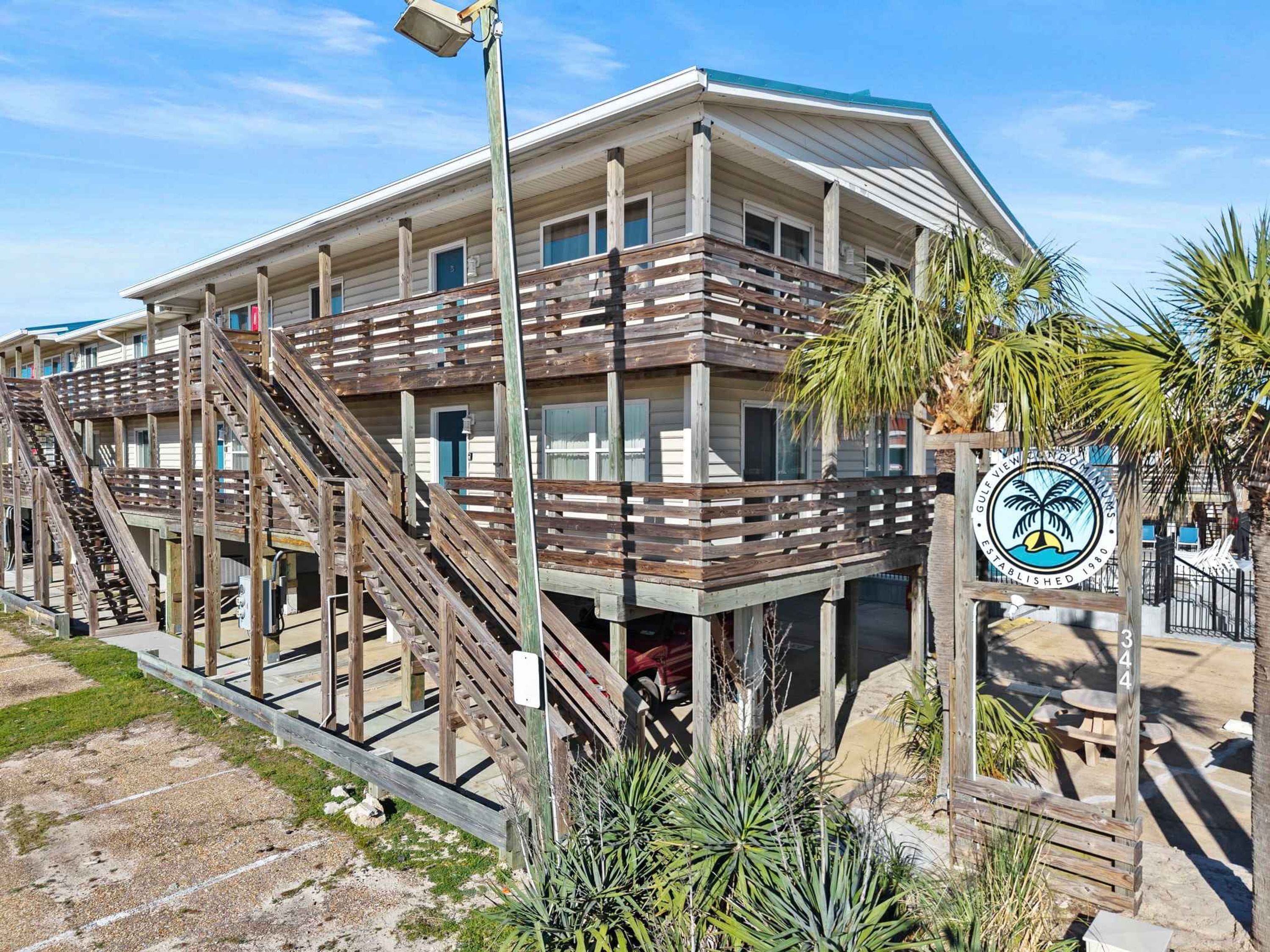 A beachfront hotel with wooden balconies, a palm tree, and a sign indicating it is a Gulf View Resort.