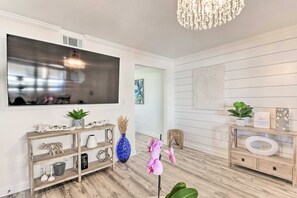 A modern living room with a large flat-screen TV, wooden console, decorative plants, and a chandelier. - Gulf Shores Beach Condo With Pool (Gulf Shores)