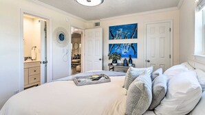 A bedroom with a bed, a ceiling fan, a door, and a wall with artwork. - Gulf Shores Beach Condo With Pool (Gulf Shores)