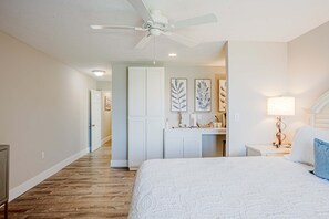 A bedroom with a bed, a ceiling fan, a nightstand, a lamp, and a hallway leading to a bathroom. - Waterfront 2-bedroom Condo in Panama City (Panama City)