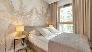 Ein Schlafzimmer mit einem Bett, zwei Nachttischlampen, einem Wandbild und einem Fenster mit Vorhängen.