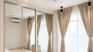 A bedroom with a large mirror, a bed, a nightstand, a chair, and a ceiling fan. - Vrindavan Staycation (Mathura)