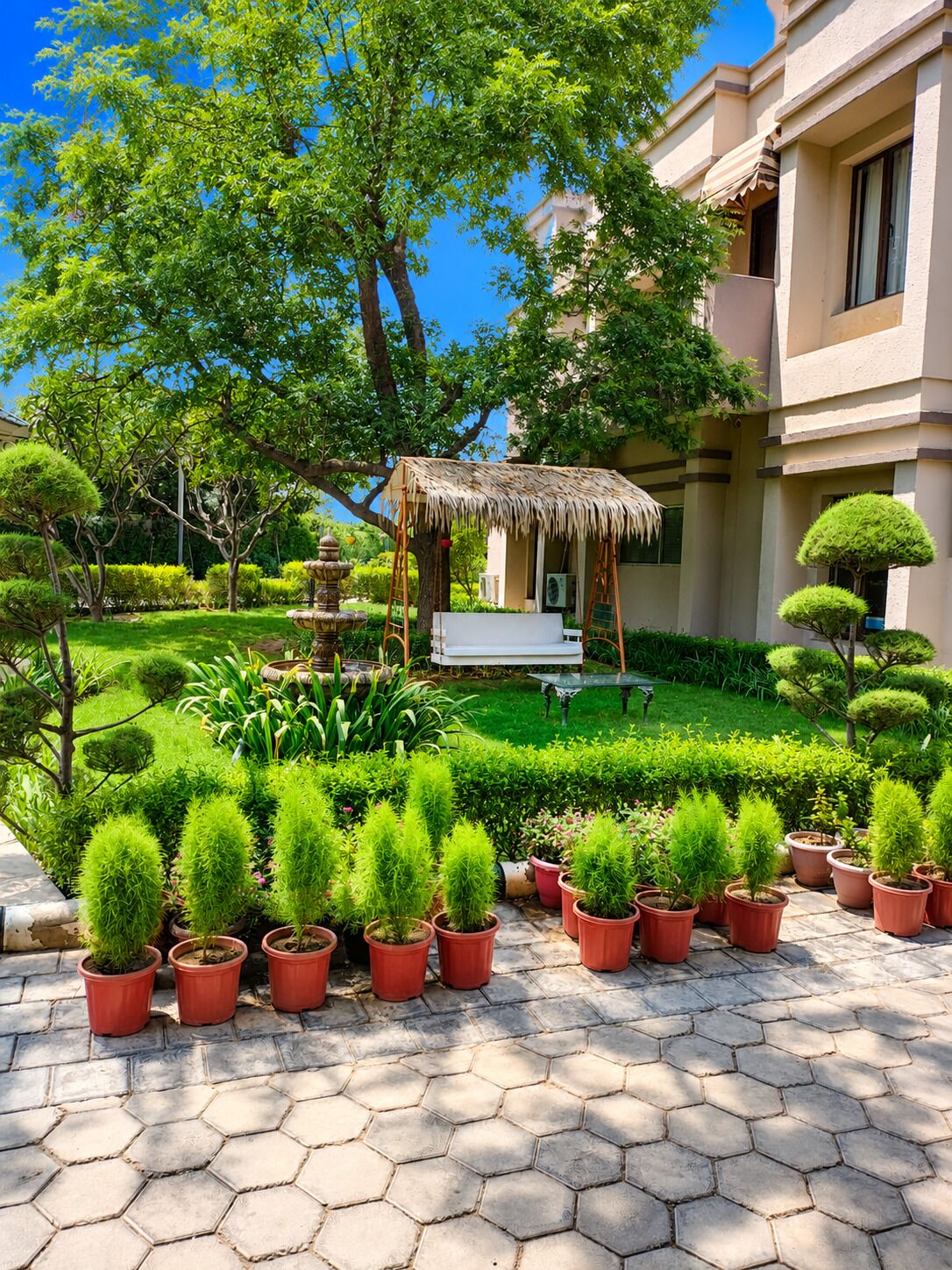 Ein Gartenbereich mit Blumentöpfen, einer Laube und einem Gebäude im Hintergrund.