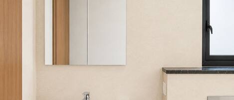 A bathroom with a white sink, a mirror, a window, and a marble countertop.