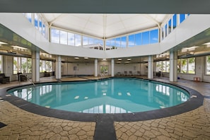 Ein beheiztes Hallenbad mit Fliesenboden, großen Fenstern und hoher Decke.