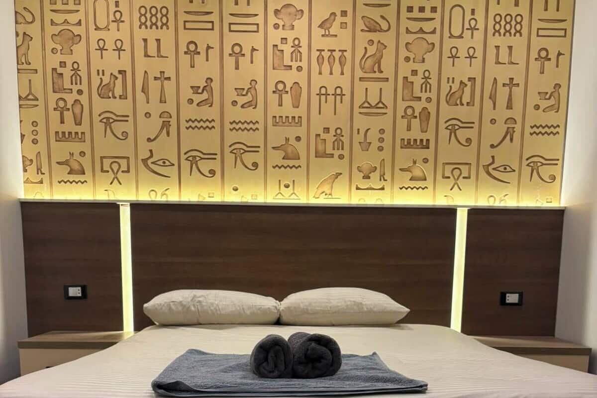 A bed with a white sheet, two pillows, and a rolled towel.