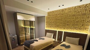 Une chambre d’hôtel avec deux lits, un minibar, une armoire fermée par des parois de verre et un mur orné d’hiéroglyphes.