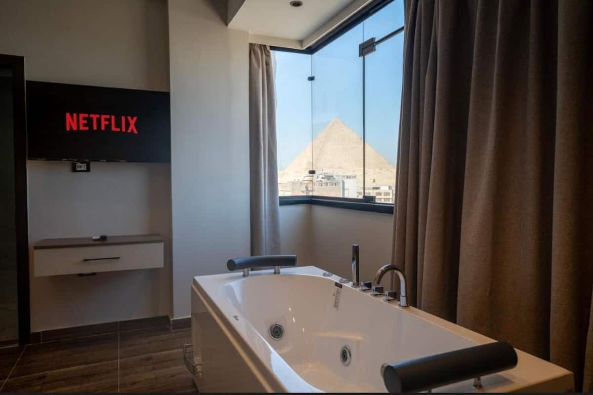 A modern bathroom with a large bathtub, a Netflix sign, and a view of a pyramid.