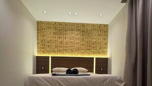 Une chambre à coucher avec un lit, un mur orné d’hiéroglyphes, un tapis et une paire de chaussures.