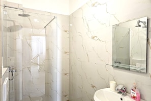 Ein modernes Badezimmer mit Duschkabine aus Glas, einem weißen Waschbecken mit Spiegel darüber und einer Wand mit Marmoroptik.