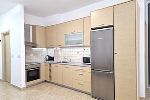 Eine moderne Küche mit Holzschränken, einem Edelstahlkühlschrank, einer Mikrowelle und einem Backofen.
