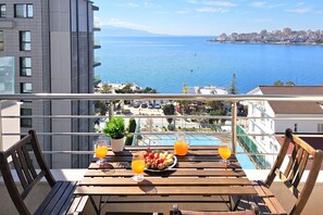 A balcony with a table set for breakfast, overlooking a coastal cityscape. - Two Bedroom Apartment With Sea View-021 (Sarandë)