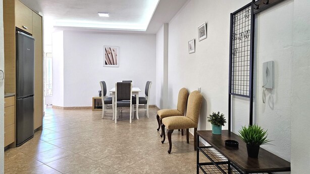 Une cuisine moderne équipée d’un réfrigérateur, un coin repas avec des chaises et une table, et un couloir avec un porte-manteau et une plante en pot.