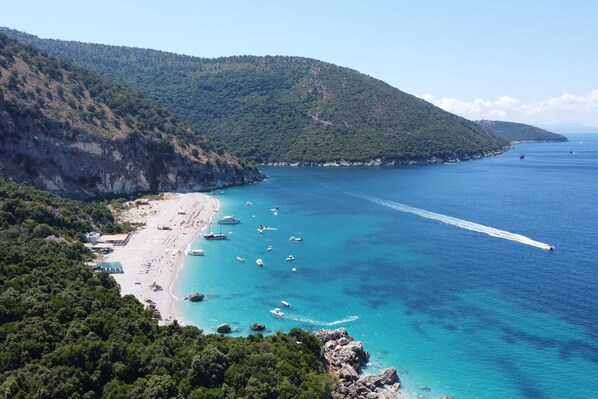 Eine Küstenansicht mit Strand, Booten und einem Bergpanorama im Hintergrund.