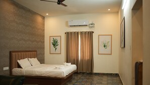 A hotel room with a bed, a ceiling fan, an air conditioner, patterned wallpaper, and a tiled floor.