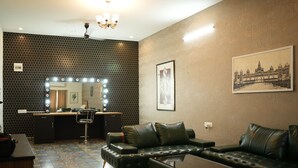 A living room with a sofa, a coffee table, a mirror with lights, a patterned wall, and a framed picture.