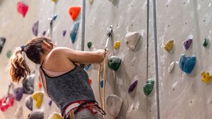 A person climbing a rock wall with various colored holds.