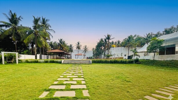 A pathway leading to a white building with a red roof, surrounded by palm trees and a grassy area.